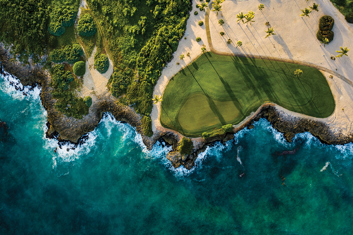 An aerial view of  beautiful green golf course with sand traps surrounded by blue ocean