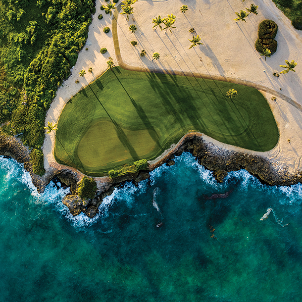 An aerial view of  beautiful green golf course with sand traps surrounded by blue ocean)