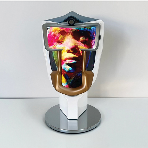 A futuristic, white head-shaped device with a gold-colored faceplate. A holographic image of a woman's face appears within the device.