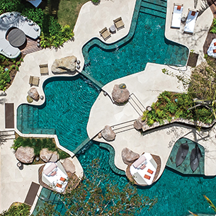 Aerial view of luxurious resort’s large swimming pool with a deck, lounge chairs and palm trees surrounding the pool 