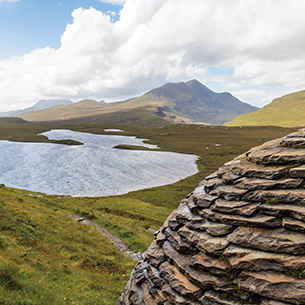 A dramatic cliff face in Scotland, where ancient Moine schists rest surprisingly on top of younger limestone, showcasing a unique geological landscape. The crag itself is a rugged slope with exposed rock layers.