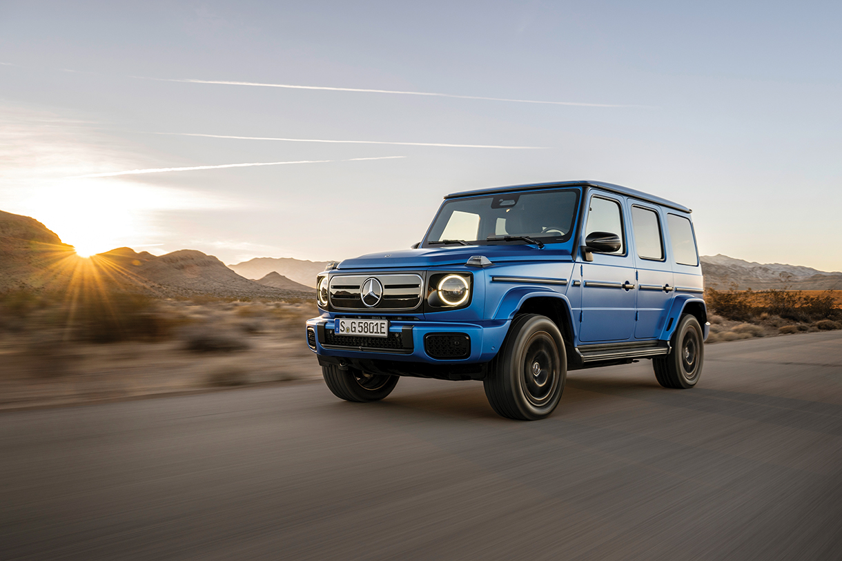 A blue Mercedes-Benz G-580 Wagon SUV driving on a desert road at sunset