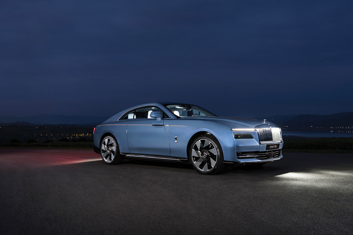 A front side view of a blue Rolls-Royce Spectre parked on the side of a road at night.