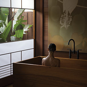 A woman relaxes in a traditional Japanese wooden bathtub, while enjoying the serene view of a lush garden through a sliding shoji screen.