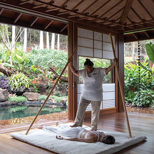 A woman receiving a walking massage in a wooden room with shoji screens opening up to an outdoor garden.