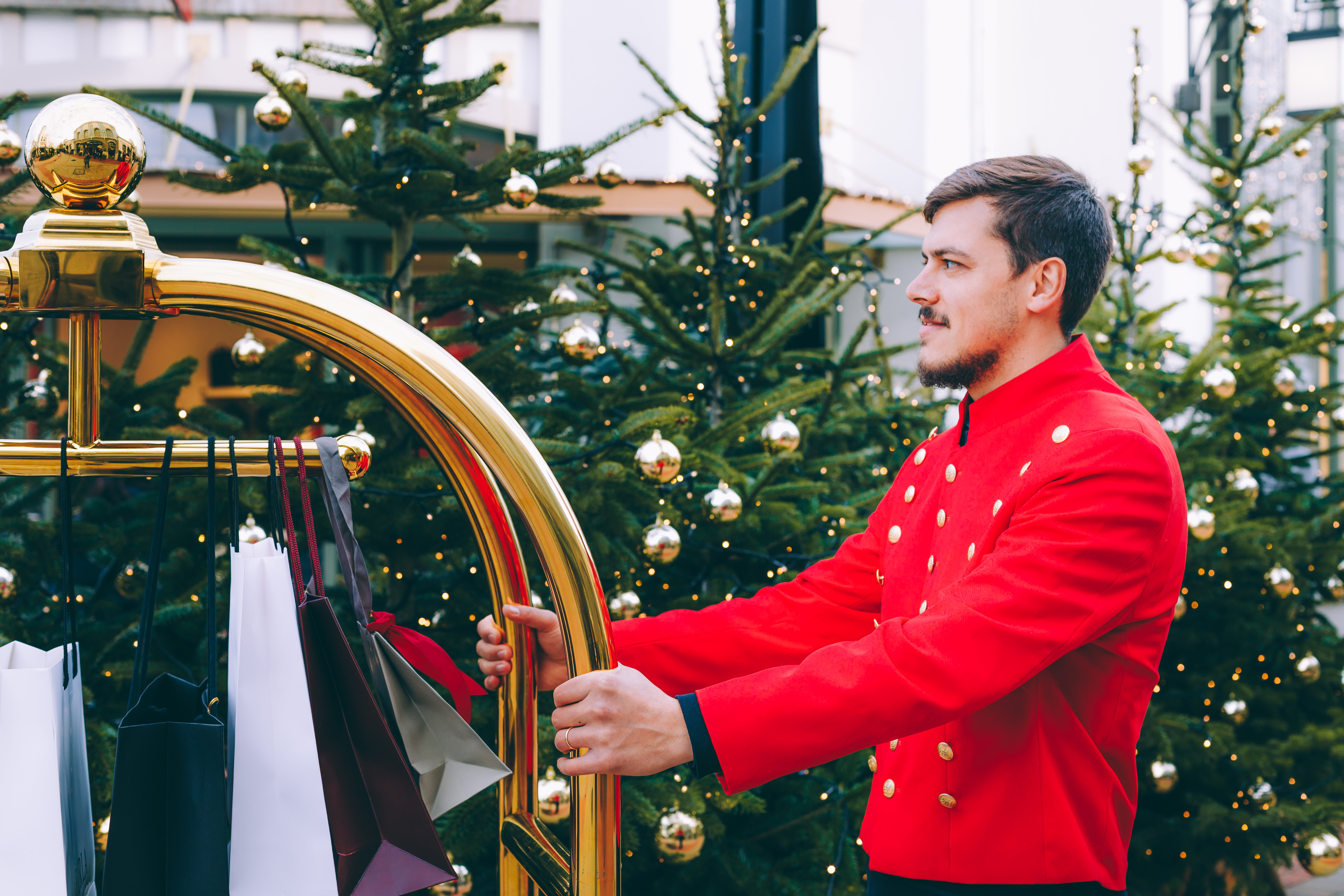 A personal valet pushing cart filled with holiday gifts with Christmas trees in the background.  Ultimate shopping experience at Fidenza Village. Concierge able to asssist in selecting holiday gifts to hands-free shopping. 