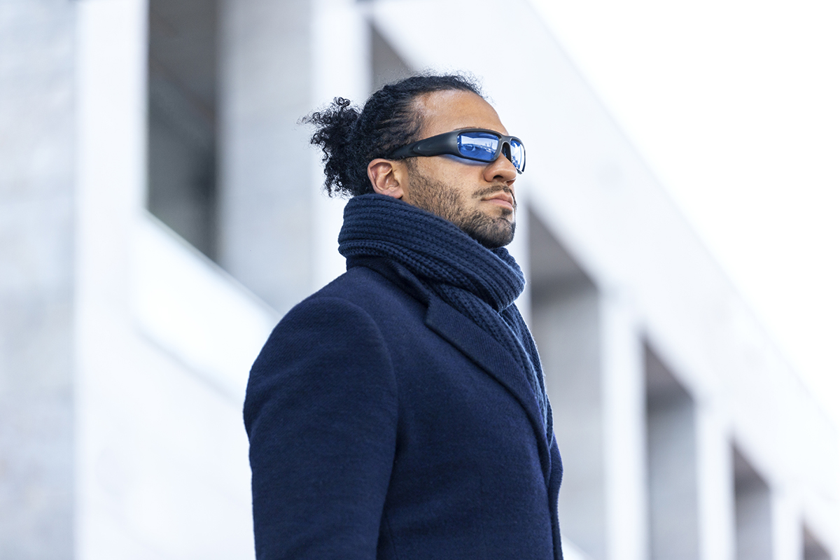 Model wearing travel glasses by Propeaq. Claims its wearable device with interchangeable blue and red lenses help control body clock and combat jet lag. App prompts user when to wear each color to dampen production of daylight chemicals in the brain or ramp up sleep-inducing hormones. 