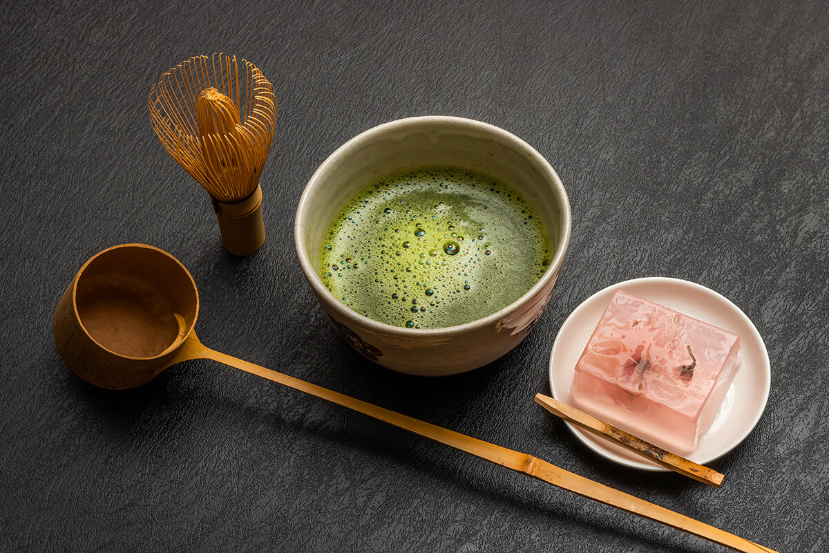 A traditional Japanese tea set with a pot of steaming green tea, a small ceramic cup, and a plate of beautifully arranged Japanese sweets called wagashi. The wagashi are colorful and have various shapes and textures, with some of them resembling flowers or leaves.