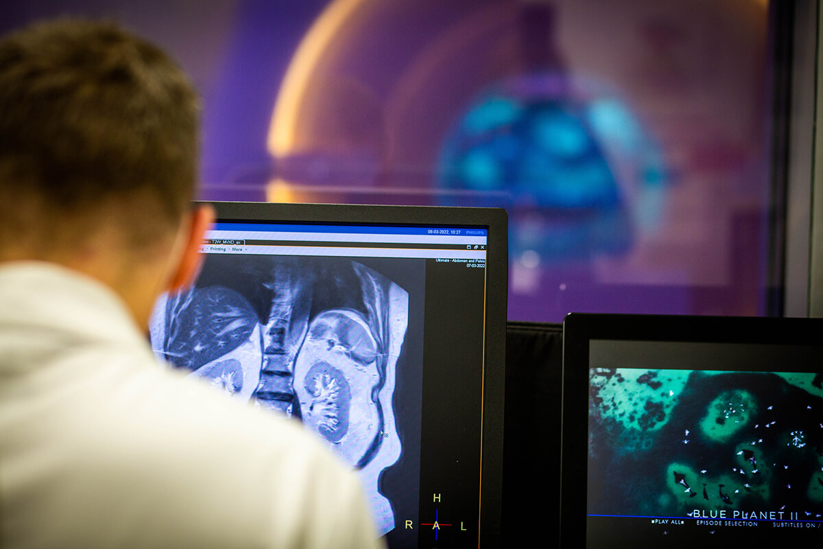 A medical setting with several black and white MRI images displayed on a computer screen. There is a medical professional wearing a white lab coat examining the images. 