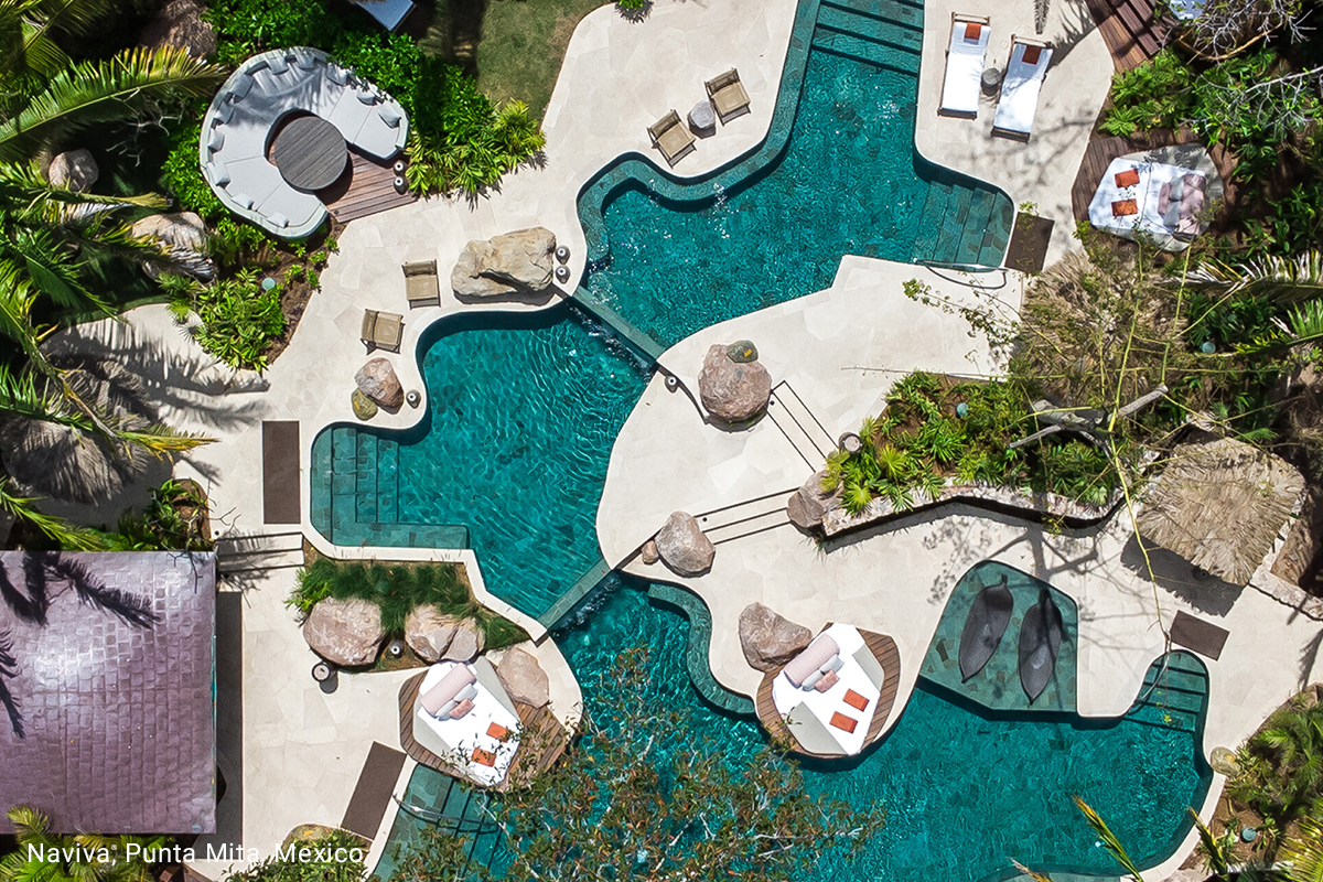 Aerial view of a swimming pool with a swim-up bar, surrounded by palm trees at Zadún, a Ritz-Carlton Reserve in San José del Cabo, Mexico.