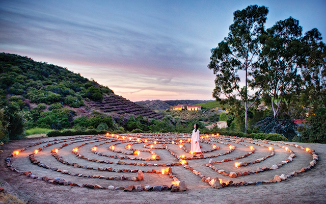 A woman standing in a circular stone labyrinth illuminated by candles