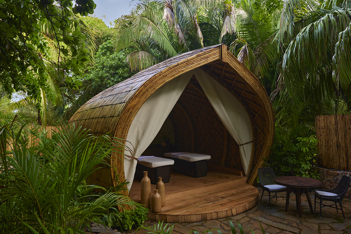 An outdoor  wooden spa hut with a curved top in a lush green tropical setting.