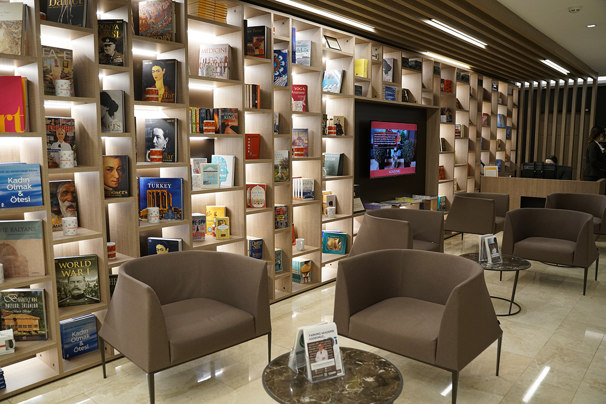 Waiting room with chairs, coffee tables and a wall with shelving full of books.