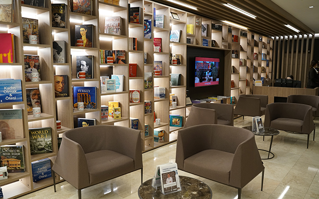 Waiting room with chairs, coffee tables and a wall with shelving full of books.