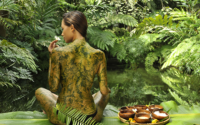 Woman with exposed back sitting in a beautiful lush green setting with a cholorophyll body wrap.